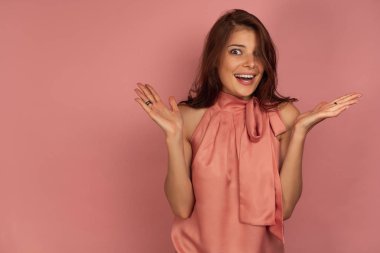 Pembe üstlü bir kız pembe bir arka plan üzerinde duruyor, ağzı açık kameraya bakıyor ve kollarını yanlara yayarak..
