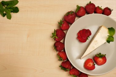 Nane dekore cheesecake bir tabak hafif ahşap bir masa üzerinde bir çerçeve kenarı ile çilek çerçeve içinde duruyor.