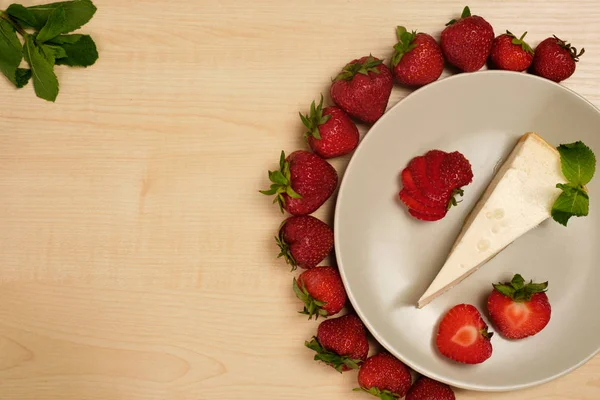 Nane dekore cheesecake bir tabak hafif ahşap bir masa üzerinde bir çerçeve kenarı ile çilek çerçeve içinde duruyor.