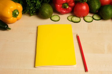 Sebzeler sarı bir not defteri üzerinde çerçevenin üst kısmında hafif bir ahşap masa üzerinde yalan.