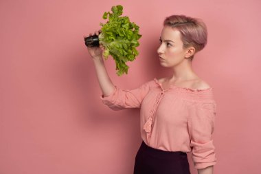 Bluz kısa pembe saçlı bir kız, pembe bir arka plan üzerinde profil ayakta, elinde bir salata düşünceli görünüyor.
