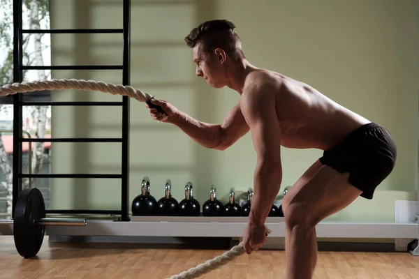 Hombre musculoso con cuerda de batalla haciendo ejercicio en el gimnasio de entrenamiento funcional. Vista del perfil . — Foto de Stock