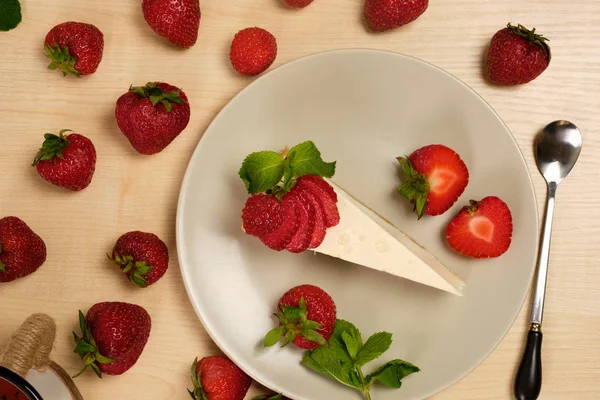 Bir tabak çilek dekore cheesecake ahşap bir masa üzerinde çilek ile çevrili duruyor