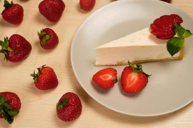 Cheesecake ve çilek ile bir tabak ahşap bir masa üzerinde çilek ile çevrili duruyor