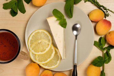 Bir fincan çay ile bir tabak üzerinde Cheesecake parlak ahşap bir masa üzerinde otlar ve kayısı ile çevrilidir