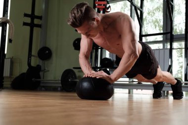 Çıplak gövdeli kaslı adam spor salonunda bir topa sıkıyor.