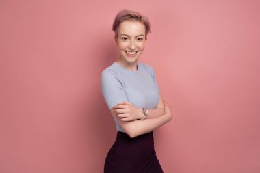 Bir t-shirt ve etek kısa pembe saçlı bir kız pembe bir arka plan üzerinde yarı açık duruyor ve kameraya bakar.