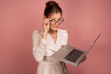 Hafif ceket ve gözlüklü kız, korkuyla dudağını ısırıyor, kameraya bakıyor, elinde bir dizüstü bilgisayar tutuyor..