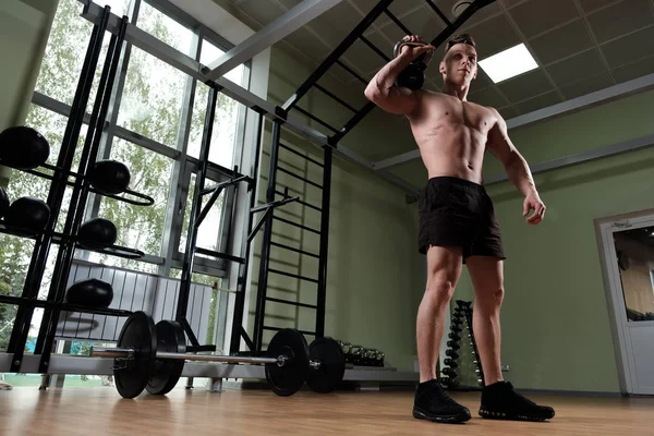 Un tipo musculoso con un torso desnudo sostiene un peso sobre su hombro, inclinando la cabeza mientras está de pie en el gimnasio, foto abajo . — Foto de Stock