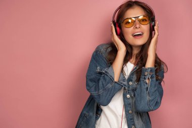 Kot pantolon ve gözlüklü güzel bir kız neşeyle kulaklıkla müzik dinliyor..