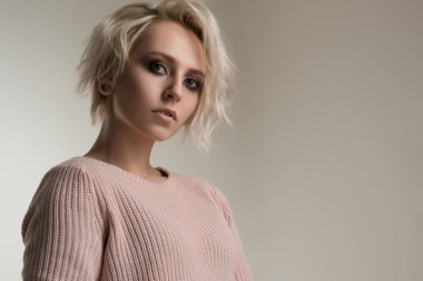 Parlak makyaj ve kısa beyaz saçlı güzel kız pembe bir kazak beyaz bir arka plan üzerinde duruyor ve çerçeve içine bakar