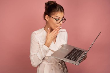 Hafif ceket ve gözlüklü bir kız dizüstü bilgisayar ile duruyor, onun avuç içi ile ağzını kapsayan, dizüstü bilgisayar sürpriz görünüyor