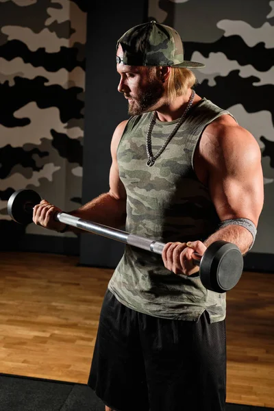Muskulöser Mann in T-Shirt und Baseballmütze hält die Langhantel in angewinkelten Armen, vertikaler Rahmen — Stockfoto