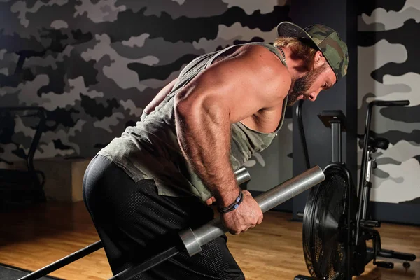 Muskulöser Mann in Sportuniform macht eine Übung auf seinen Schultern, nach vorne gebeugt, Geier in den Händen, horizontales Foto — Stockfoto