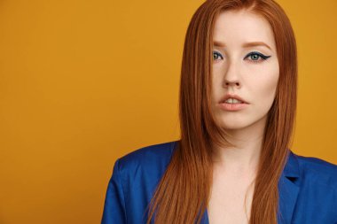 Sarı arka planda duran düz saçlı, uzun okları olan, mavi ceketli, kızıl saçlı bir kızın portresi.