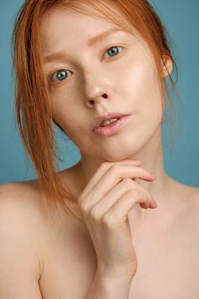 Ett nära porträtt av en rödhårig flicka med ren strålande hud, blå ögon och ingen makeup, stöttande hakan på handen Stockbild