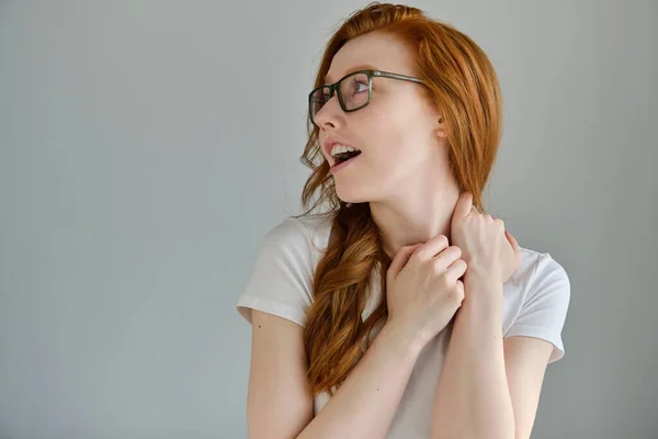 Das rothaarige Mädchen in weißem T-Shirt und Brille schaut freudig weg und öffnet den Mund. Stockbild