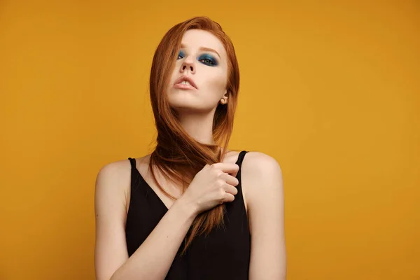 Redhead κορίτσι σε μια μαύρη κορυφή και με μπλε μακιγιάζ ματιών στέκεται σε ένα κίτρινο φόντο με το κεφάλι ρίχνονται πίσω και καλύπτονται με τρίχες — Φωτογραφία Αρχείου