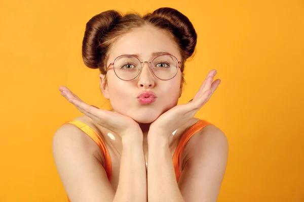 Rothaariges Mädchen mit runder Brille und orangefarbenem Oberteil steht auf gelbem Grund, das Kinn ruht auf der Handfläche, die Lippen nach vorne gestreckt — Stockfoto