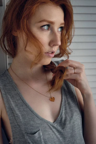 Una ragazza dai capelli rossi si alza a metà curva e guarda in lontananza, tenendo la punta di una treccia con la mano . — Foto Stock