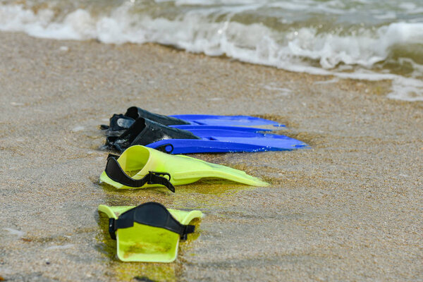 Yellow and blue flippers for diving lie on the beach in the water