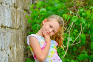 Genç ve güzel kız bir yaz elbise bir gülümseme ile sokakta bir tuğla duvara karşı poz.