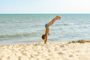 Bir kız sahilde atlar ve denize kum boyunca ellerine yürüyor