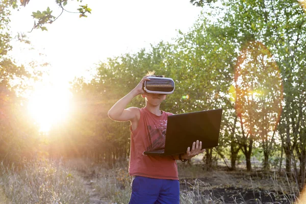 A boy on nature in virtual space, VR glasses, a forest, a laptop