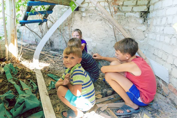 Street children sit in the trash in the corner of an abandoned house. Staged photo.