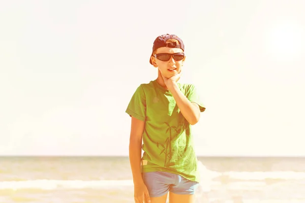 男孩戴着一顶帽子 戴着太阳镜 顶着天空 一个在沙滩上顶着大海的棒球帽的时尚男人 — 图库照片