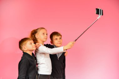 İki erkek ve bir kız bir smartphone üzerinde stüdyoda selfie yapma, pembe bir arka planda.
