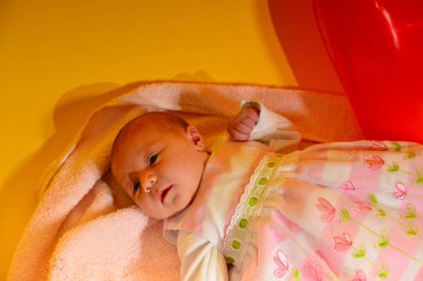 Yeni doğmuş bir bebek çocuk oyuncakları ile sarı bir arka plan üzerinde pembe bir ninni yalan söylüyor