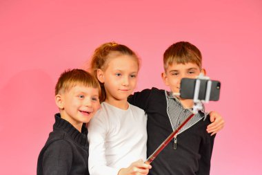 İki erkek ve bir kız bir smartphone üzerinde stüdyoda selfie yapma, pembe bir arka planda.