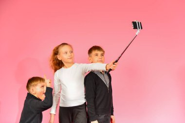 İki erkek ve bir kız bir smartphone üzerinde stüdyoda selfie yapma, pembe bir arka planda.