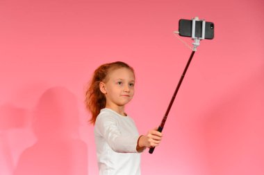 Bir kız pembe bir arka planda stüdyoda bir akıllı telefonda bir selfie alır