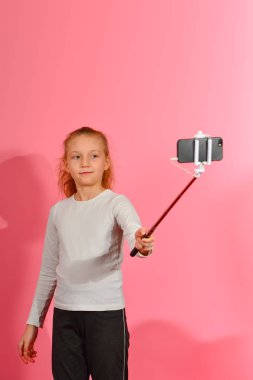 Bir kız pembe bir arka planda stüdyoda bir akıllı telefonda bir selfie alır