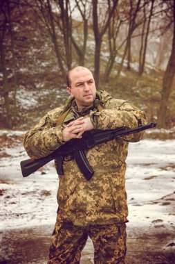 Askeri bir adam silahla duruyor.