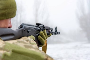 Bir askeri asker otomatik bir tüfek ile nişan alır ve kış aylarında eldivenleri içinde tutar.