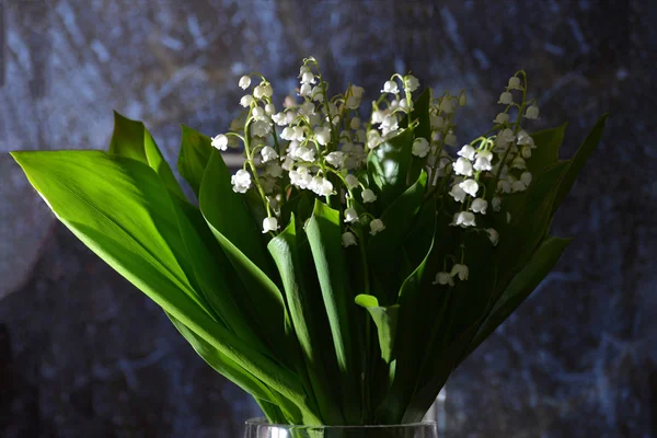 A bouquet of lilies of the valley in a glass vase, lilies of the valley on a blue marble background