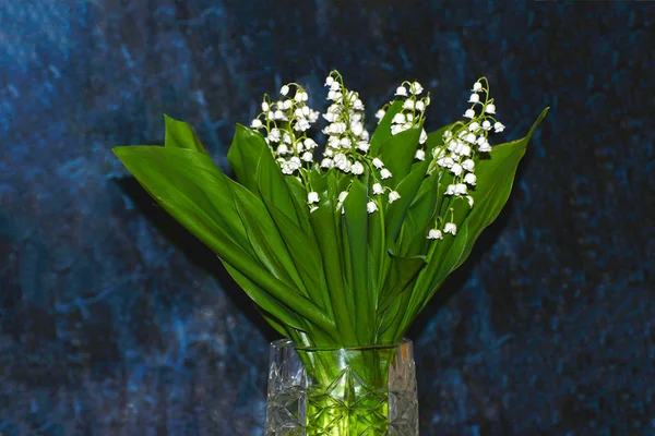 A bouquet of lilies of the valley in a glass vase, lilies of the valley on a blue marble background