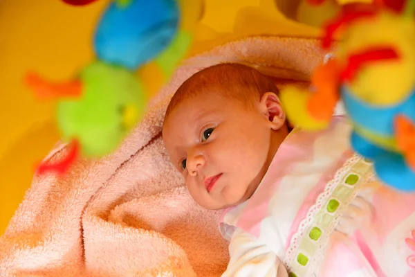 Newborn baby with hanging toys on yellow.