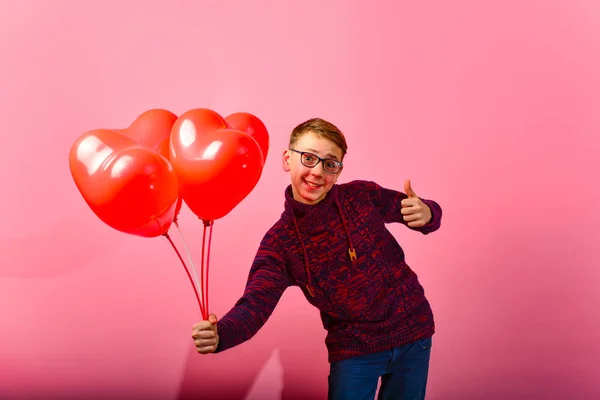 一个年轻英俊的家伙给气球在粉红色的背景心脏的形状 — 图库照片
