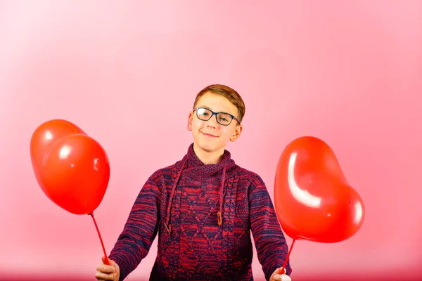 A boy holds heart-shaped balloons on a pink background.