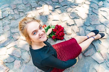 Güzel ve seksi kız bir tuğla yolu ve bir buket kırmızı gül yalan yan yana yere oturur