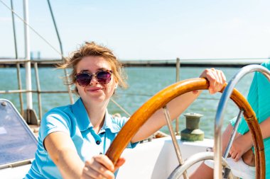 Bir kız bardaklarda etrafa bir yat güvertede tekerlek yanına oturur