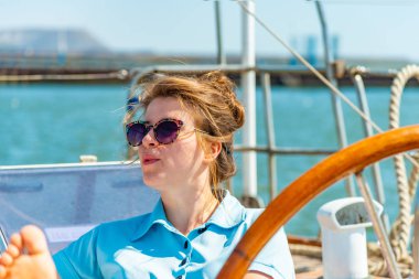 Bir kız bardaklarda etrafa bir yat güvertede tekerlek yanına oturur