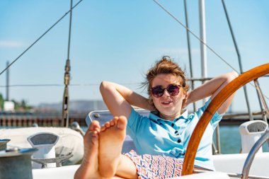 Bir kız bardaklarda etrafa bir yat güvertede tekerlek yanına oturur