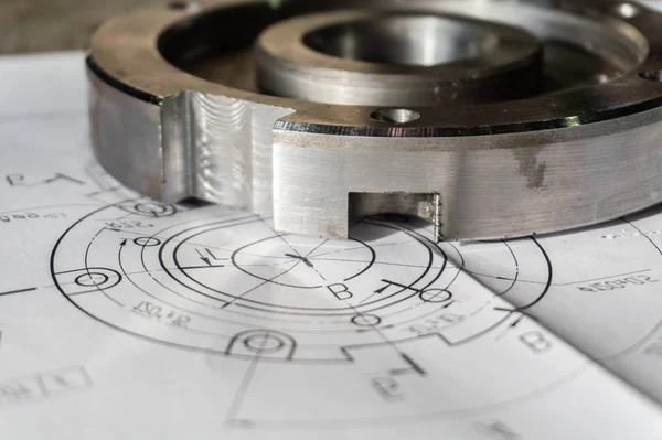 The transition flange after processing lies on the technical drawing. Detail ready to work with a drawing together in mechanical engineering