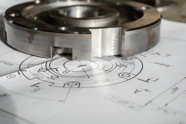 The transition flange after processing lies on the technical drawing. Detail ready to work with a drawing together in mechanical engineering