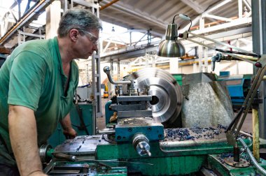 İşçi, bir adam bir makine üzerinde metal ürünler işler. Üretim çalışmalarında dönüm
